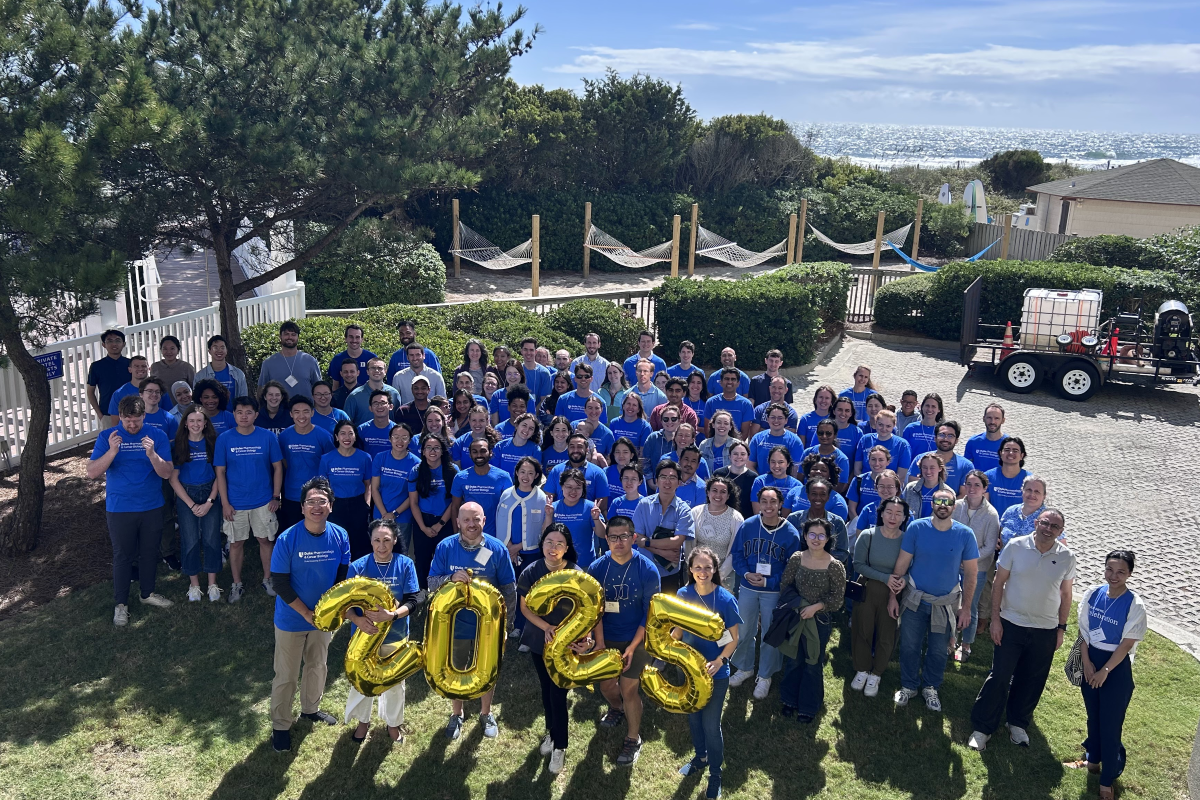 Group photo of PCB department retreat attendees standing outside on a sunny day at Wrightsville Beach. Four attendees hold gold balloons spelling out 2025.