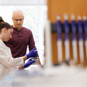 Jonathan Campbell observing gloved lab member perform experiment